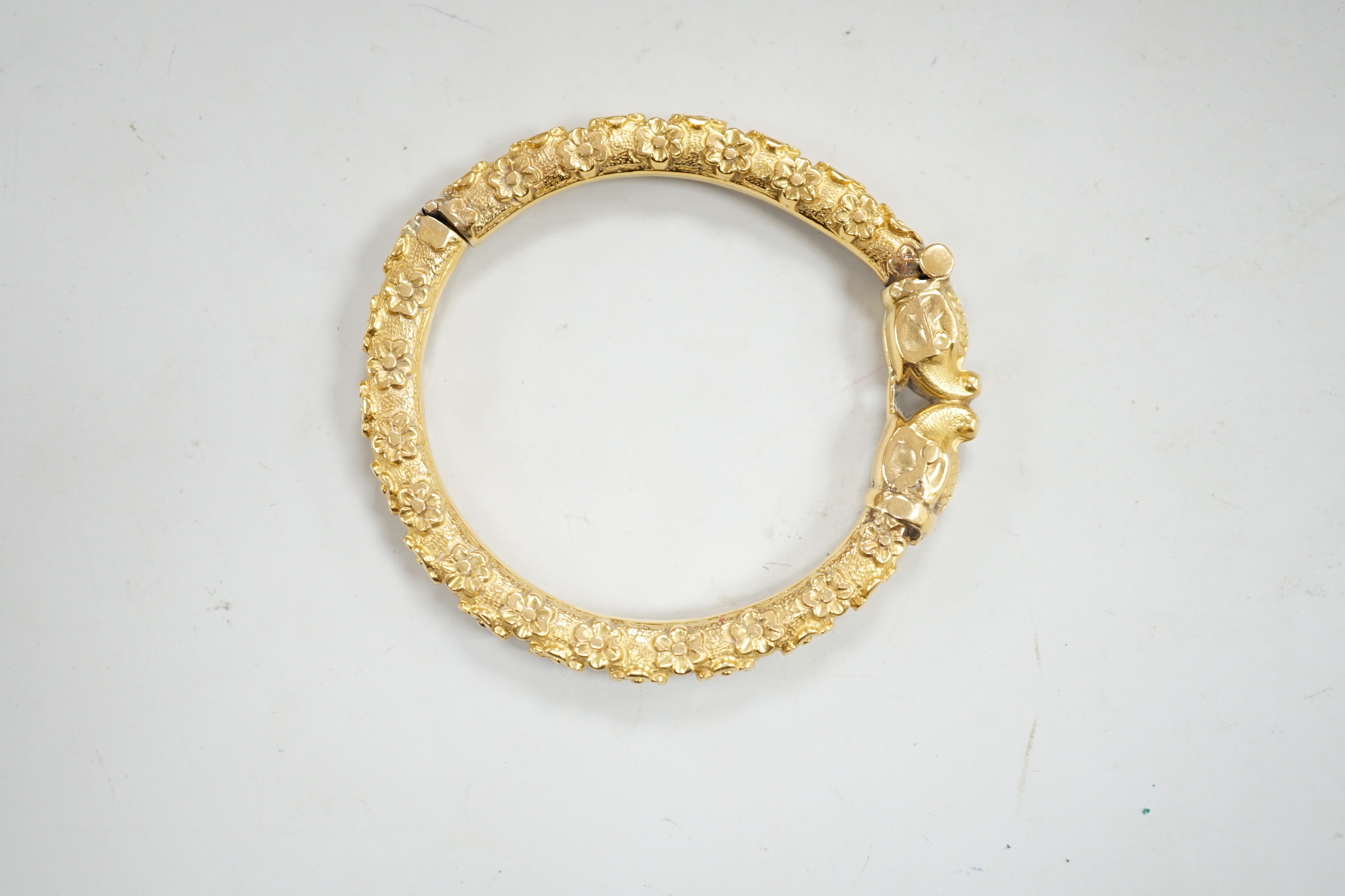 An antique yellow metal hinged bangle, with flower head decoration and dragon's? head terminals, gross weight 23.9 grams.